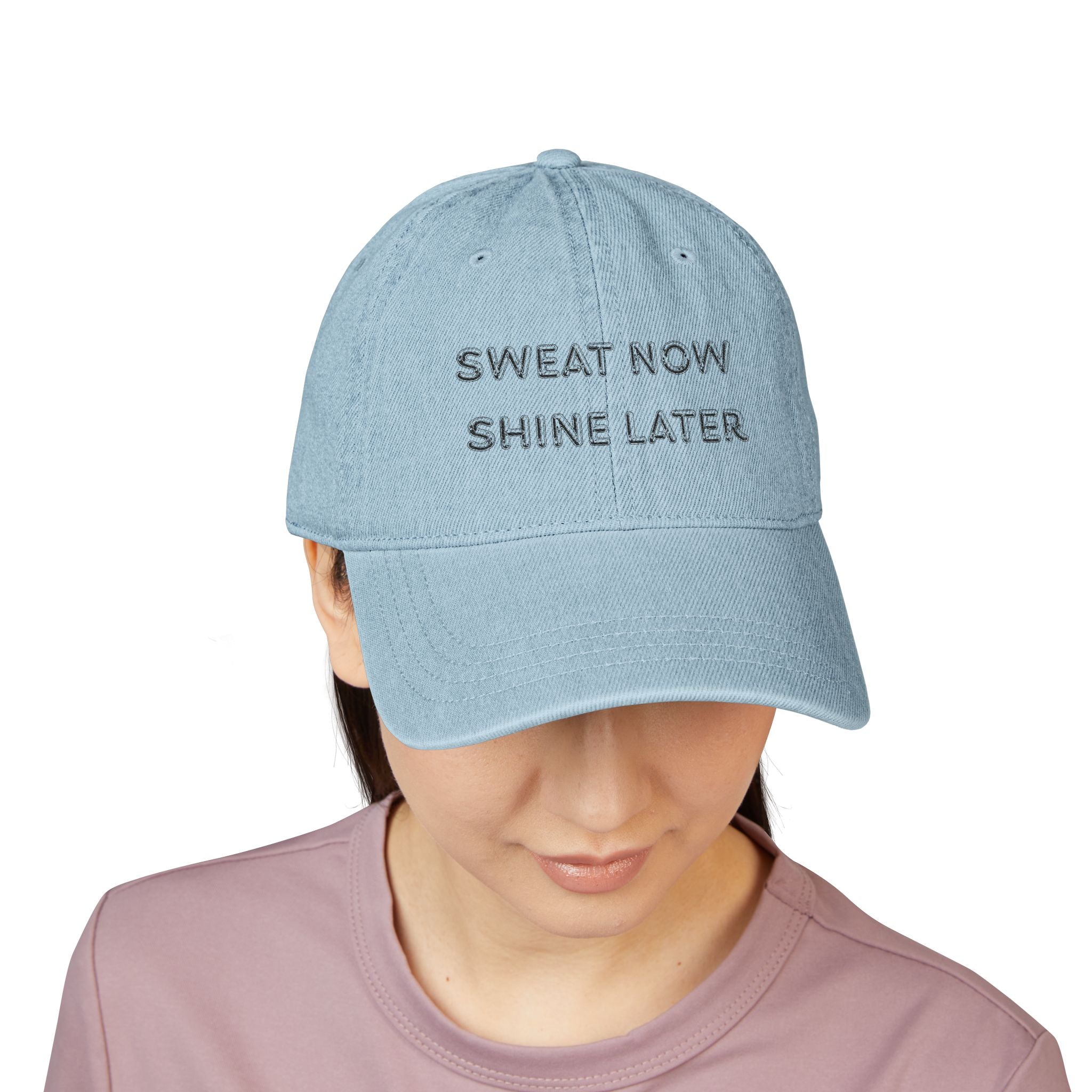 Light blue cap with 'SWEAT NOW SHINE LATER' text worn by a person on a white background