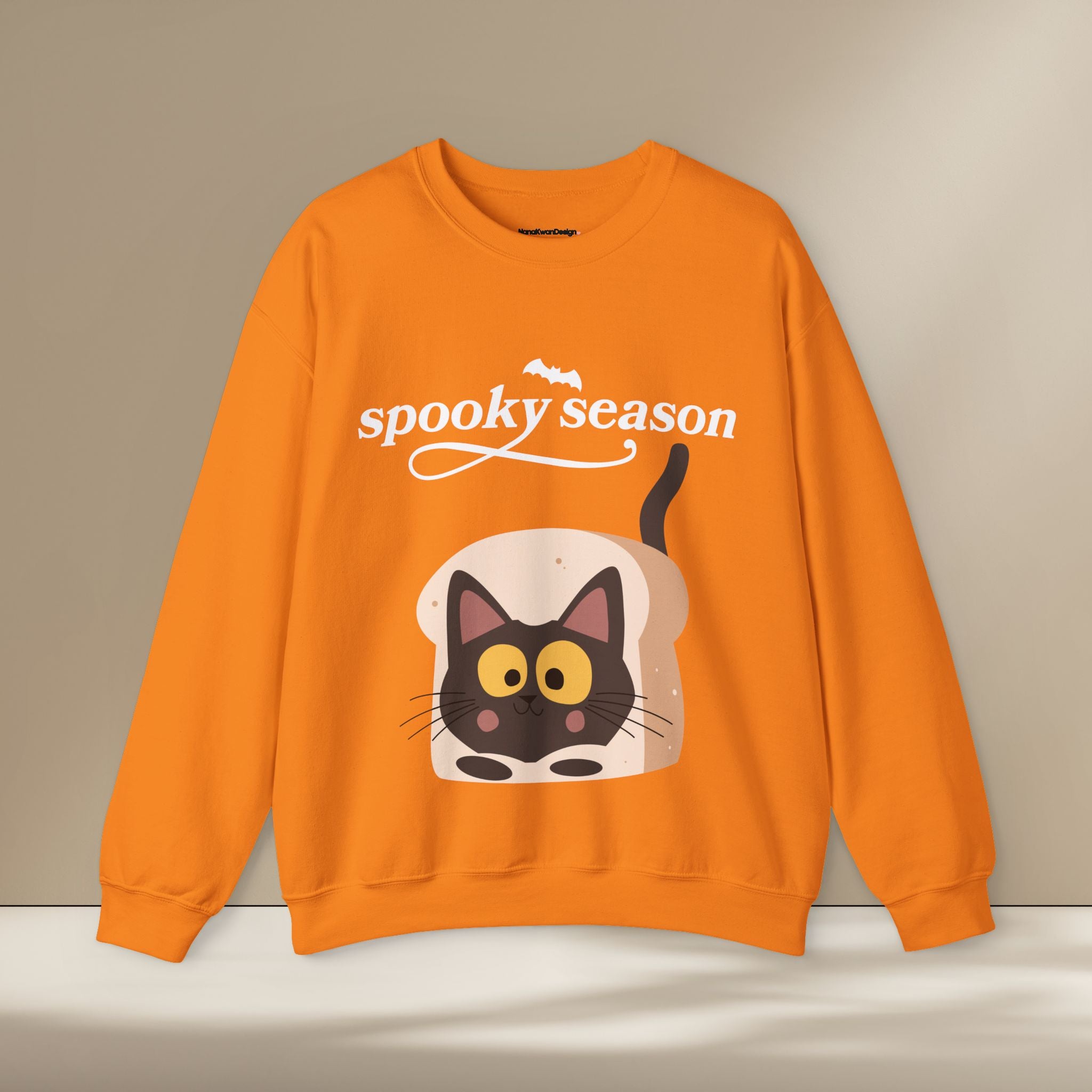 Orange sweatshirt with a cat design and 'spooky season' text on a beige background