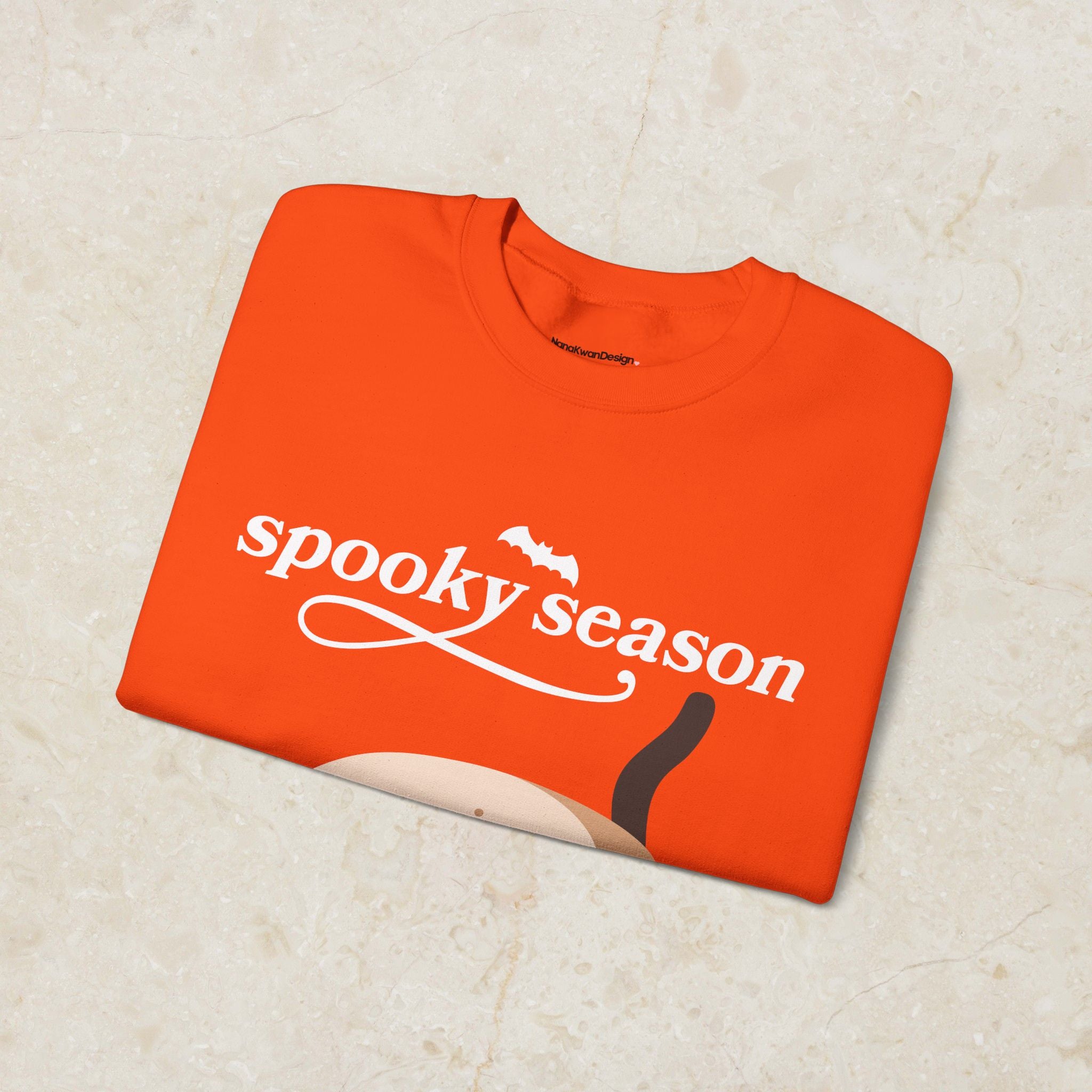 Folded orange sweatshirt with 'spooky season' text on a beige surface