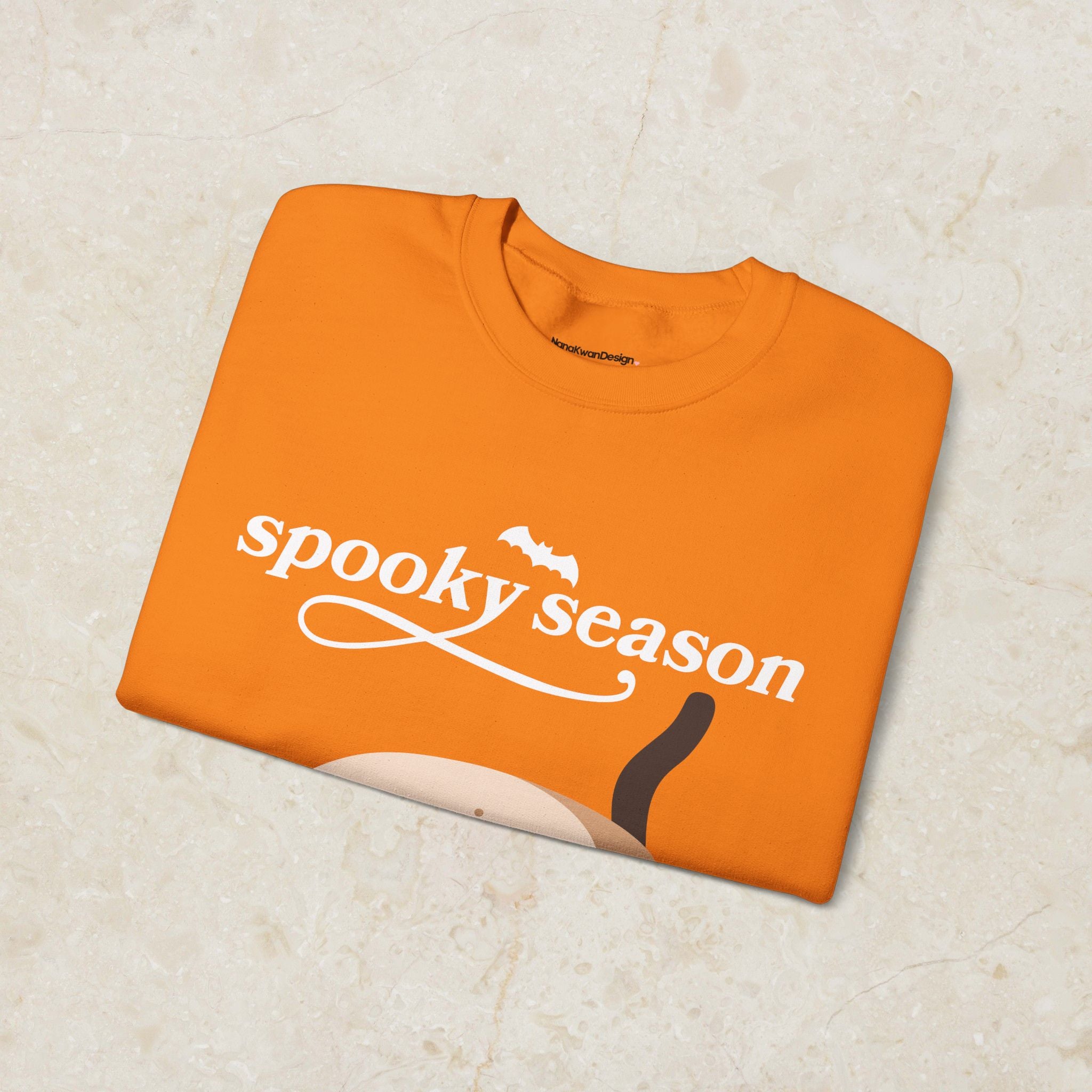 Orange sweatshirt with 'spooky season' text on a beige surface